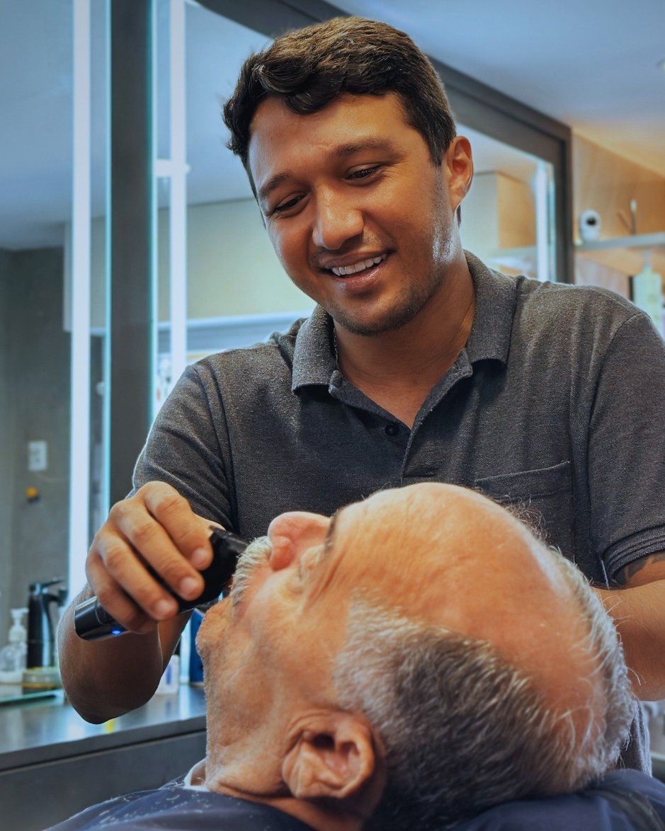 Barbeiro da Dom Bigode sorrindo enquanto acerta a barba de um cliente de cabelo branco