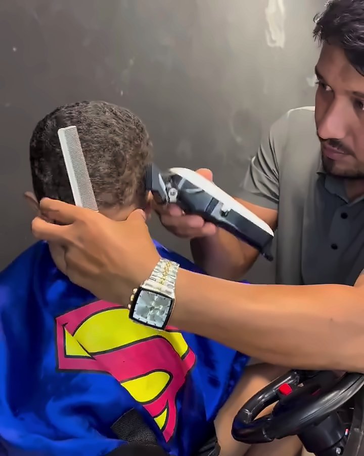 Corte infantil na cadeira de carrinho, com a criança de capa de super-herói