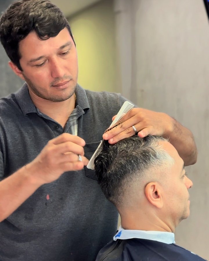 Barbeiro penteando o topo de um degradê