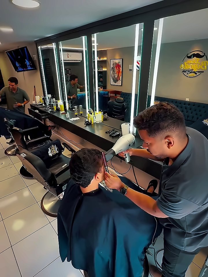 Barbeiro cortando o cabelo de um cliente, com os espelhos iluminados do salão